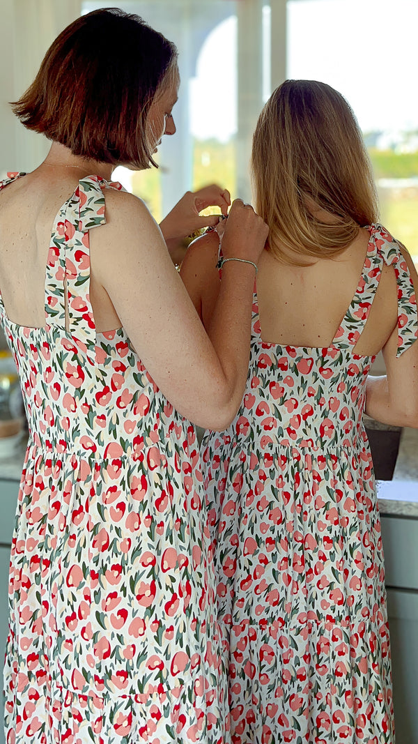 Two young caucasian women wearing pink & red floral Maven Maxi Sundress as one ties the other's shoulder tie