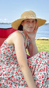 Young caucasian women sitting in front of the ocean wearing sunhat and pink & red Maven Maxi sundress