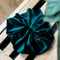 Soft velvet oversized scrunchie in deep teal with out of focus leaf