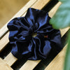 Soft velvet oversized scrunchie in dark navy with out of focus leaf