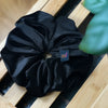 Soft velvet oversized scrunchie in black with out of focus leaf